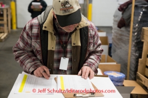 Checking over the packing list paperwork at the Airland Transport's sort facility as volunteers sort and package people food & accompanying supplies for the trail volunteers to eat during the race at the 20+ checkpoints on Friday February 14, 2014.  Iditarod Sled Dog Race 2014PHOTO BY JEFF SCHULTZ/IDITARODPHOTOS.COM  USE ONLY WITH PERMISSION