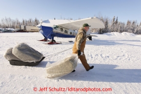 February 16, 2013  Volunteer John Hooley slides 3 bales of hay toward an airplane headed to Rainy Pass at the Willow airport as musher food, straw, HEET and people food is flown to the 4 checkpoints on the east side the Alaska Range. Photo Copyright Jeff Schultz  -- Do not reproduce without written permission