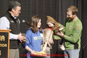 Thursday February 28, 2013  14th month old Rosie Maximer, daughter of musher Kelley Maximer picks her fathers starting number from a mukluk held by Hannah O'Toole, a child from the Make a Wish Foundation and sponsored by Donlin Gold, whose General Manager Stan Foo looks on at the musher drawing banquet held at the Dena'ina Convention Center in Anchorage two days prior to the start of Iditarod 2013.Photo (C) Jeff Schultz/IditarodPhotos.com  Do not reproduce without permission