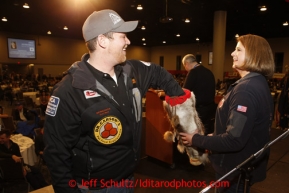 Thursday February 28, 2013  Musher Jake Berkowitz draws his starting postion from a mukluk held by principal sponsor Karen Hagedorn of ExxonMobil at the musher drawing banquet held at the Dena'ina Convention Center in Anchorage two days prior to the start of Iditarod 2013.Photo (C) Jeff Schultz/IditarodPhotos.com  Do not reproduce without permission