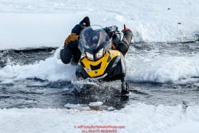 One of the Iditarod Insider film crew, Ian Planchen, drives his snowmachine across the open water of the Happy River on the trail in Ptarmigan Valley on the way to Rohn from the Rainy Pass checkpoint during Iditarod 2016.  Alaska.  March 07, 2016.  Photo by Jeff Schultz (C) 2016 ALL RIGHTS RESERVED