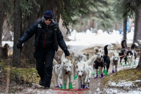 Volunteer checker Lisa Jaeger leads Rob Cooke's team out of its parking spot and onto the trail at the Rohn checkpoint during Iditarod 2016.  Alaska.  March 08, 2016.  Photo by Jeff Schultz (C) 2016 ALL RIGHTS RESERVED