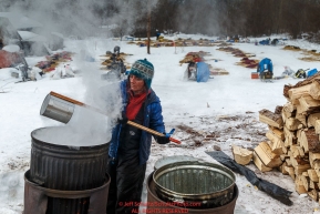 Michelle Phillips gets boiling water from a community cook pot for her dogs at the Takotna checkpoint during Iditarod 2016.  Alaska.  March 09, 2016.  Photo by Jeff Schultz (C) 2016  ALL RIGHTS RESERVED