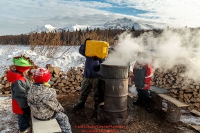 Takotna resident students pour water into a heat pot for mushers at the Takotna checkpoint during Iditarod 2016.  Alaska.  March 09, 2016.  Photo by Jeff Schultz (C) 2016  ALL RIGHTS RESERVED