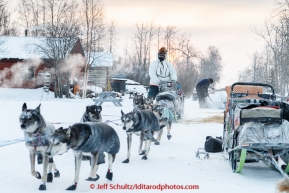 Steve Watkins runs down the road and past teams parked on the banks of the Yukon river at the Tanana checkpoint as the sun rises behind him at 20 below zero on Wednesday morning March 11th during the 2015 Iditarod.(C) Jeff Schultz/SchultzPhoto.com - ALL RIGHTS RESERVED DUPLICATION  PROHIBITED  WITHOUT  PERMISSION