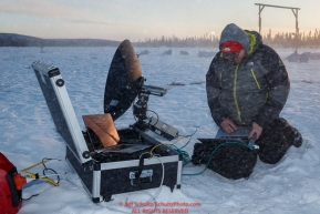 Jeff's trail assistant, Deroy Brandt, uploads images outdoors on a fast remote satellite dish at the Cripple checkpoint on Thursday March 10 during Iditarod 2016.  Alaska.    Photo by Jeff Schultz (C) 2016  ALL RIGHTS RESERVED