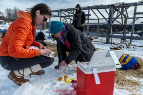 P-Team members Grace Bolt (Left) and Leoni Ballard collect urine samples from Hugh Neff's team at the Ruby Checkpoint during the 2016 Iditarod.  March 11, 2016   Photo by Jeff Schultz (C) 2016  ALL RIGHTS RESERVED