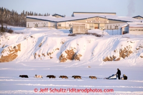 John Baker on the Bering Sea with the Elim school in the background shortly after leaving the Elim checkpoint on Tuesday March 12, 2013.Iditarod Sled Dog Race 2013Photo by Jeff Schultz copyright 2013 DO NOT REPRODUCE WITHOUT PERMISSION