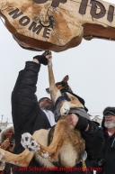 Justin Savidas touches his lead dogs' paw holding a special coin on the burl arch finish line in a memorial gesture to the late Omer Chartrand, the father of an Iditarod Insider editor at Nome on Thursday March 13 during the 2014 Iditarod Sled Dog Race.PHOTO (c) BY JEFF SCHULTZ/IditarodPhotos.com -- REPRODUCTION PROHIBITED WITHOUT PERMISSION