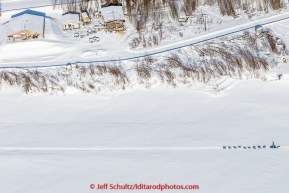 A team runs down the Yukon river past buildings on his way into Galena in the afternoon on Thursday March 12, 2015 during the 2015 Iditarod (C) Jeff Schultz/SchultzPhoto.com - ALL RIGHTS RESERVED DUPLICATION  PROHIBITED  WITHOUT  PERMISSION