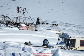 Ketil Reitan runs down the Yukon River past a fish-wheel and boats on the bank as he approaches the Nulato checkpoint on Saturday March 12th during the 2016 Iditarod.  Alaska    Photo by Jeff Schultz (C) 2016  ALL RIGHTS RESERVED