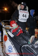 Wednesday March 14, 2012     Aaron Burmeister 's son Hunter sits on his dads' sled as Aaron is interviewed in the finish chute shortly after Aaron arrived Nome. Iditarod 2012.