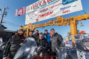 The Iditarod Trail Breakers pose for a photo under the arch in Nome on Tuesday March 15th during the 2016 Iditarod.  Alaska    Photo by Jeff Schultz (C) 2016  ALL RIGHTS RESERVED