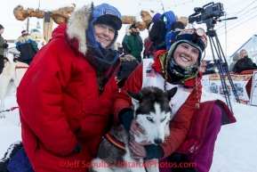 Lisbet Norris gives her lead dog Ruby a hug in the finish chute shorlty after finishing in 48th at Nome.  With her is her mother Kari Skogen who ran her first race 30 years ago. Saturday March 15 during the 2014 Iditarod Sled Dog Race.PHOTO (c) BY JEFF SCHULTZ/IditarodPhotos.com -- REPRODUCTION PROHIBITED WITHOUT PERMISSION