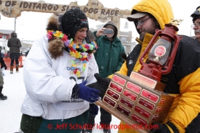 Christine Roalofs, who finished in last place and is winner of the Red Lantern Award, is presented the award by race sponsor representative Scott A Johnson of Wells Fargo at the finish line on Front Street in Nome.  Iditarod Sled Dog Race 2013Photo by Jeff Schultz copyright 2013 DO NOT REPRODUCE WITHOUT PERMISSION