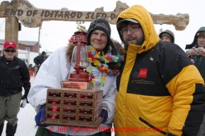 Christine Roalofs, who finished in last place and is winner of the Red Lantern Award, is presented the award by race sponsor representative Scott A Johnson of Wells Fargo at the finish line on Front Street in Nome.  Iditarod Sled Dog Race 2013Photo by Jeff Schultz copyright 2013 DO NOT REPRODUCE WITHOUT PERMISSION