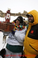 Christine Roalofs, who finished in last place and is winner of the Red Lantern Award, is presented the award by race sponsor representative Scott A Johnson of Wells Fargo at the finish line on Front Street in Nome.  Iditarod Sled Dog Race 2013Photo by Jeff Schultz copyright 2013 DO NOT REPRODUCE WITHOUT PERMISSION