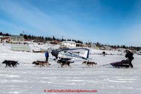 Jessie Royer runs past volunteer pilot Jerry Wortley and plane as she arrives in the afternoon at the White Mountain checkpoint on Tuesday March 16, 2015 during Iditarod 2015.  (C) Jeff Schultz/SchultzPhoto.com - ALL RIGHTS RESERVED DUPLICATION  PROHIBITED  WITHOUT  PERMISSION