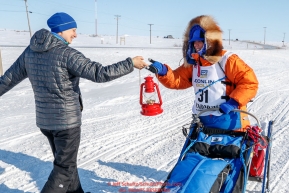 Former Nome resident and Iditarod finisher, Melissa Stewart, gives last place finisher and Red Lantern Award winner Cindy Abbott the red lantern on the outskirts of Nome on her way to the finish line during the 2017 Iditarod on Saturday March 18, 2017.Photo by Jeff Schultz/SchultzPhoto.com  (C) 2017  ALL RIGHTS RESERVED