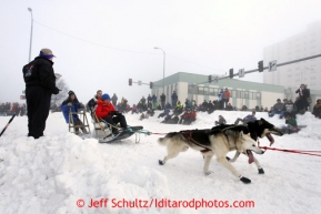 Longtime volunteer crossing guard, Angie Slingluff, mans her post at the Cordova Street turn as Travis Beals runs by during the Ceremonial start of the Iditarod sled dog race Anchorage Saturday, March 2, 2013. Photo (C) Jeff Schultz/IditarodPhotos.com  Do not reproduce without permission