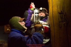 Mary Helwig at the Nome finish line extinquishes the Widow's lamp with the help of Leo Rasmusson after she finished  the 2016 Iditarod.  Alaska    

Photo by Jeff Schultz (C) 2016  ALL RIGHTS RESERVED