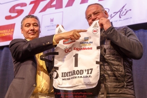 Iditarod board member Danny Seybert and Iditarod CEO Stan Hooley hold up a #1 bib with an honorary symbol