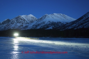 A team streaks across the glare ice of the Tatina River on the way to Rohn a dusk with the Alaska Range in the background