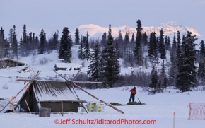 Tuesday March 6, 2012  Volunteer Dale Peterson rakes hay in the early morning as the sun breaks on the Alaska Range at the Rainy Pass checkpoint, Iditarod 2012.