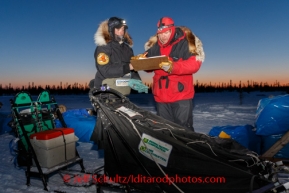 Jim Gallea checks in Pete Kaiser 's team at dusk at the Cripple checkpoint, Thursday, March 6, during the Iditarod Sled Dog Race 2014.PHOTO (c) BY JEFF SCHULTZ/IditarodPhotos.com -- REPRODUCTION PROHIBITED WITHOUT PERMISSION