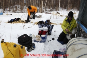 Skytrekking Alaska pilot and guide Tim Gossett prepares a hot lunch meal for his guests at the halfway checkpoint of Iditarod as Martin Buser feeds his dogs on Thursday March 7, 2013.Iditarod Sled Dog Race 2013Photo by Jeff Schultz copyright 2013 DO NOT REPRODUCE WITHOUT PERMISSION