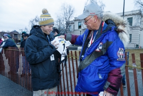 Musher Alan Stevens gets his bib from volunteer Jim Johnson in the staging area during the cermonial start day of Iditarod 2015. Saturday March 7, 2015(C) Jeff Schultz/SchultzPhoto.com - ALL RIGHTS RESERVED DUPLICATION  PROHIBITED  WITHOUT  PERMISSION