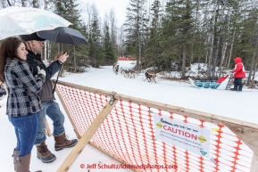 Kristen Swift and Cory Williams use umbrellas to shield themselves from the rain as they watch Aaron Burmeister run past them along the Campell Creek trails during the cermonial start day of Iditarod 2015 in Anchorage, Alaska. Saturday March 7, 2015(C) Jeff Schultz/SchultzPhoto.com - ALL RIGHTS RESERVED DUPLICATION  PROHIBITED  WITHOUT  PERMISSION