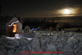 Friday March 9, 2012  the Communications tent is lit up and surrounted by mushers food drop bags as a full moon lights the sky of  the half-way checkpoint at Cripple.   Iditarod 2012.