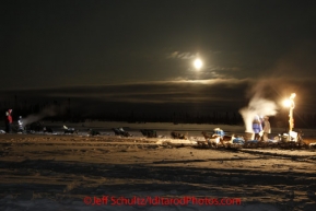 Friday March 9, 2012   5-time Iditarod champion Rick Swenson stops to check in with volunteer Bill Gallea under a full moon at the half-way checkpoint at Cripple.  Jim Gallea holds Rick's leaders.   Iditarod 2012.