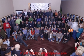 The entire field of 66 2013 Iditarod mushers pose for a group photo during a toast by the Millenium Alaska Hotel manager Carol Fraser. The photo was taken during the mandatory musher meeting at the Millenium hotel two days prior to the start of Iditarod 2013.Photo (C) Jeff Schultz/IditarodPhotos.com  Do not reproduce without permission