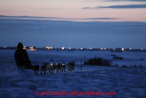 Cim Smyth runs on the trail with the lights of the  Unalakleet checkpoint in back ground on his way in on Sunday March 10, 2013.