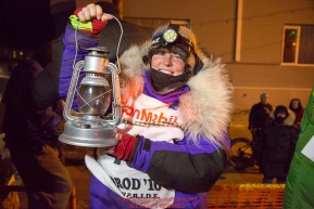 Mary Helwig at the Nome finish line holds up the Widow's lamp during the 2016 Iditarod.  Alaska    Photo by Jeff Schultz (C) 2016  ALL RIGHTS RESERVED